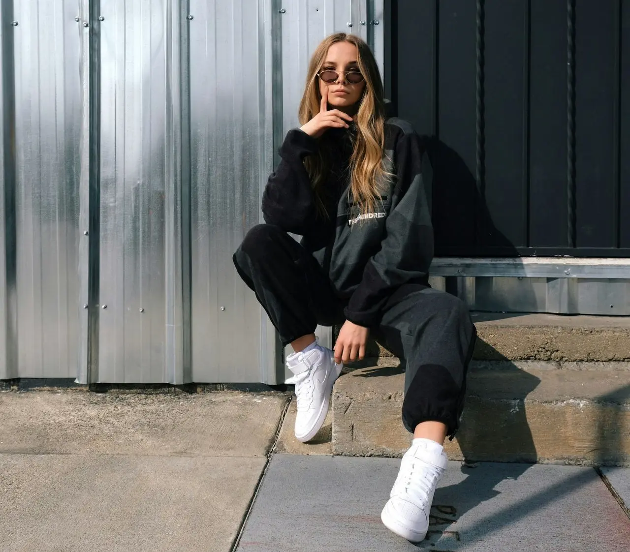 woman in black jacket and white pants sitting on gray concrete floor