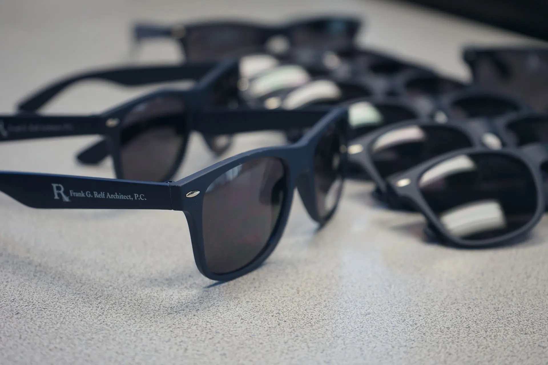 A collection of custom-branded sunglasses with the logo 'R. Frank G. Relf Architect, P.C.' printed on the side. This image showcases personalized promotional items designed to enhance brand visibility and leave a lasting impression.