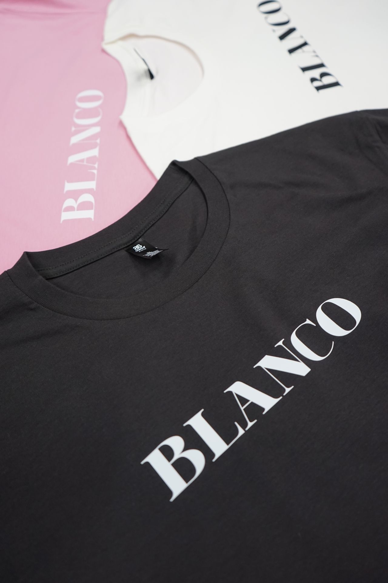 Elegant 'BLANCO' t-shirts in black and pink, featuring bold white lettering for a striking contrast. This minimalist design captures the essence of the brand, combining simplicity with a strong visual impact