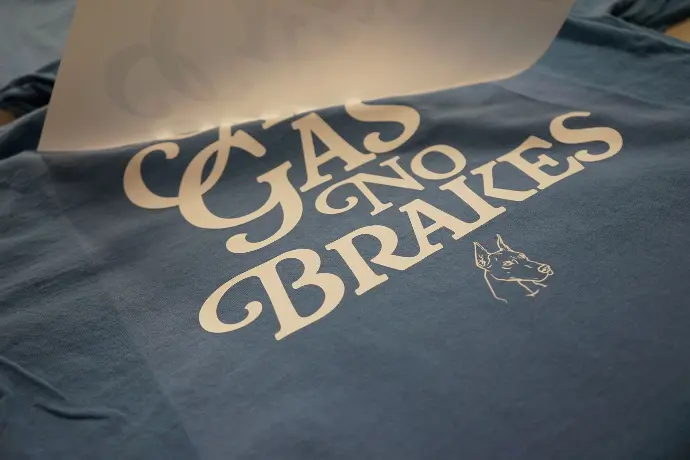 A freshly printed 'All Gas No Brakes' graphic T-shirt, showcasing stylish cursive lettering alongside a unique dog illustration. This design embodies a bold, adventurous spirit, perfect for expressing a go-getter attitude and a love for unique, statement apparel.