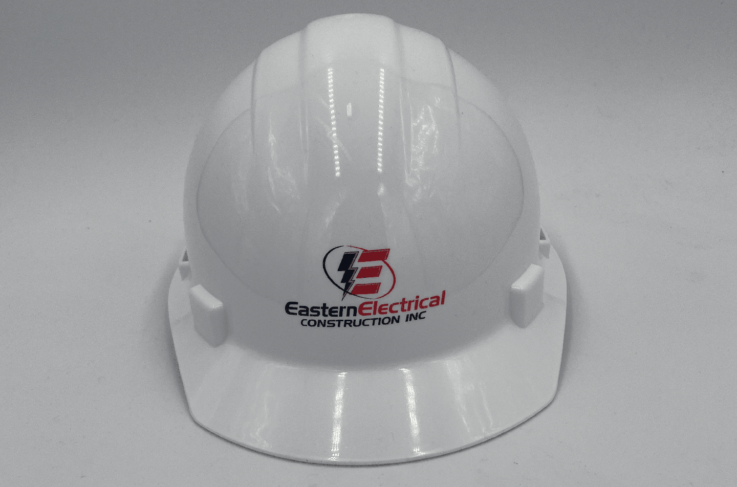 Professional white hard hat showcasing the Eastern Electrical Construction Inc. logo. The safety helmet is detailed with a striking lightning bolt graphic, emphasizing the electrical focus of the company. This essential piece of personal protective equipment is designed to provide both safety and brand identity on the job site.