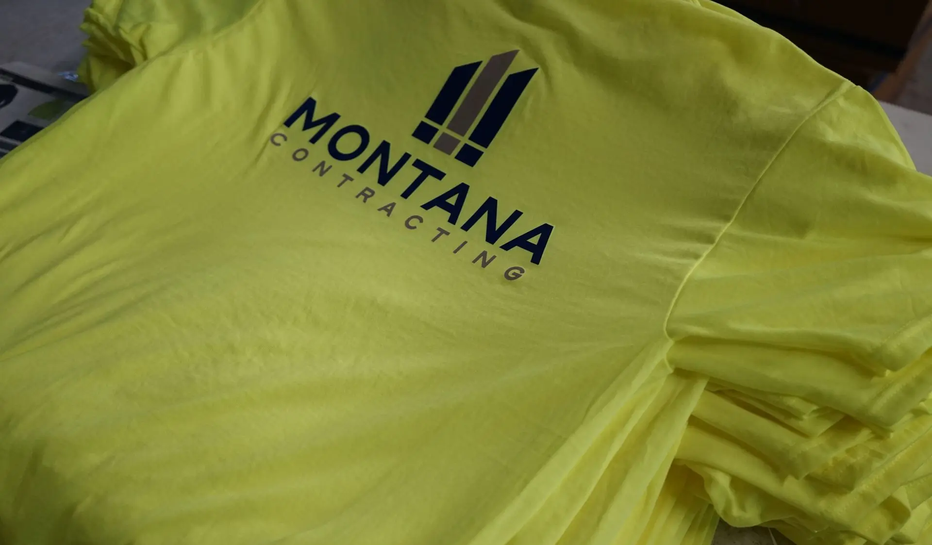 Bright yellow high-visibility safety shirt with the 'MONTANA CONTRACTING' logo prominently displayed. The shirt's vivid color ensures worker visibility on-site, while the logo in navy blue provides a professional representation of the Montana Contracting brand, known for its commitment to safety and quality in construction services.