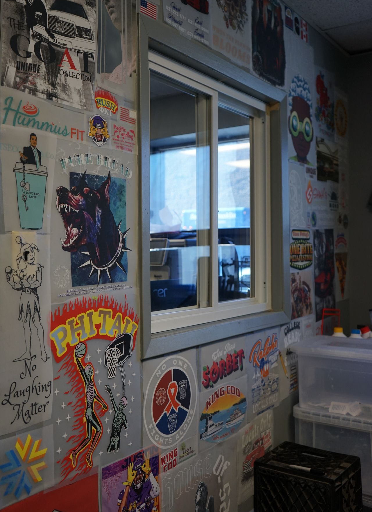 A creative workspace adorned with a diverse collection of custom Direct to Film prints. This wall, showcasing vibrant and unique graphics, reflects the breadth of personalized branding solutions offered, from whimsical illustrations to bold logos, illustrating the versatility and creativity in custom apparel and merchandise.